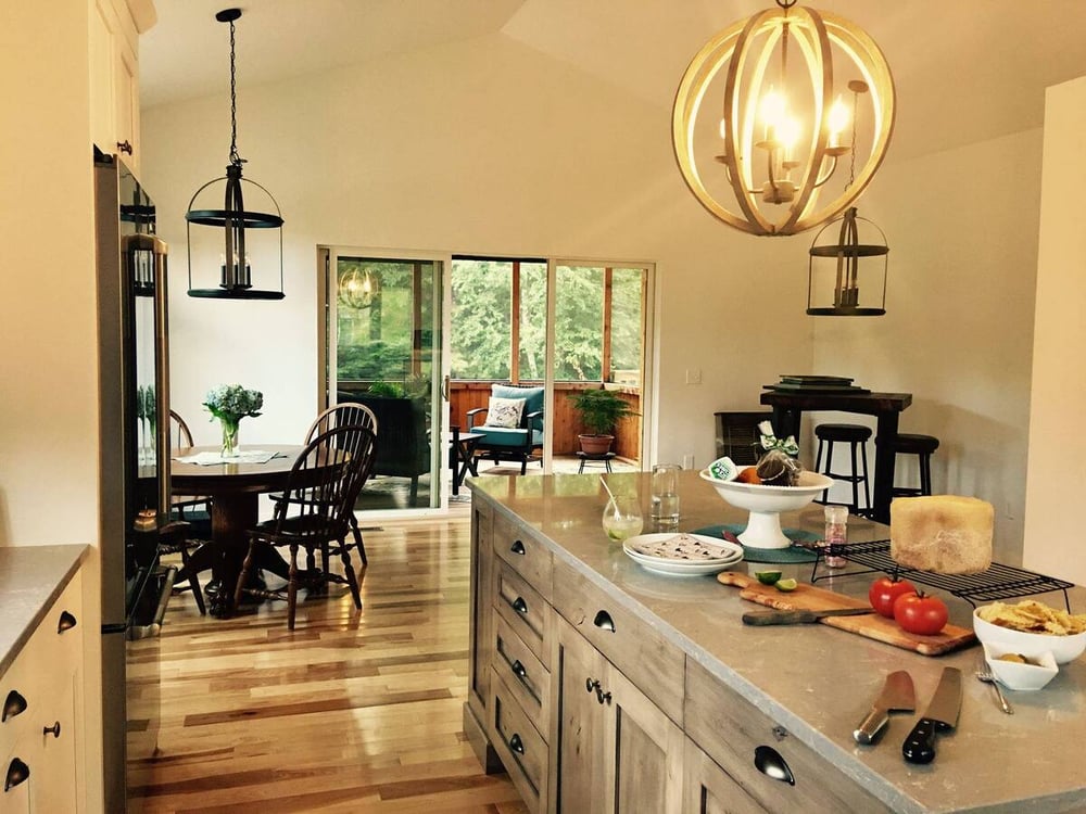 Circular light fixture above island with storage in New Hampshire kitchen remodel with sliding glass door open to porch