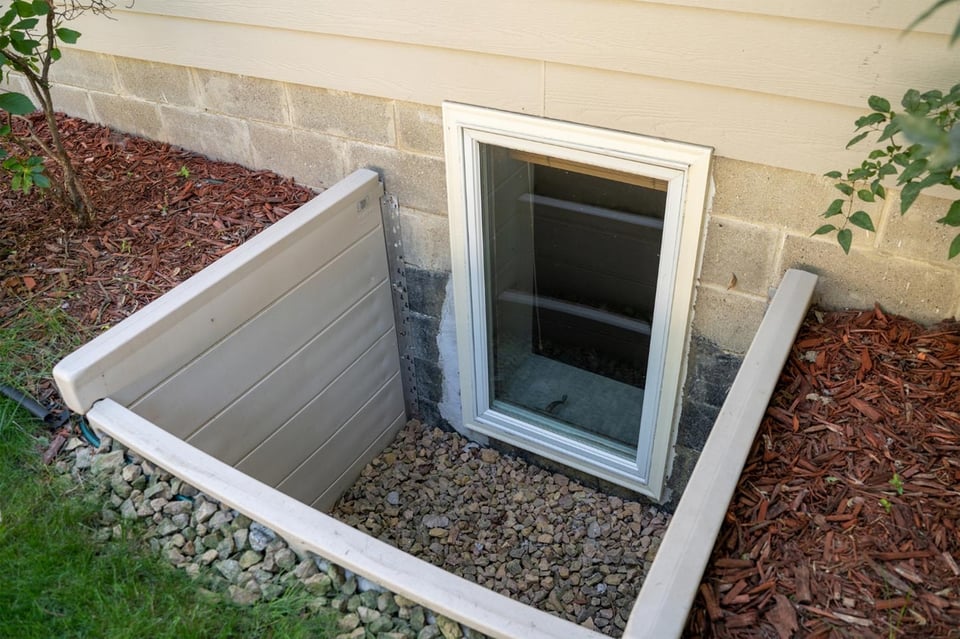Egress window installation with white frame and gravel base by Oxland Builders