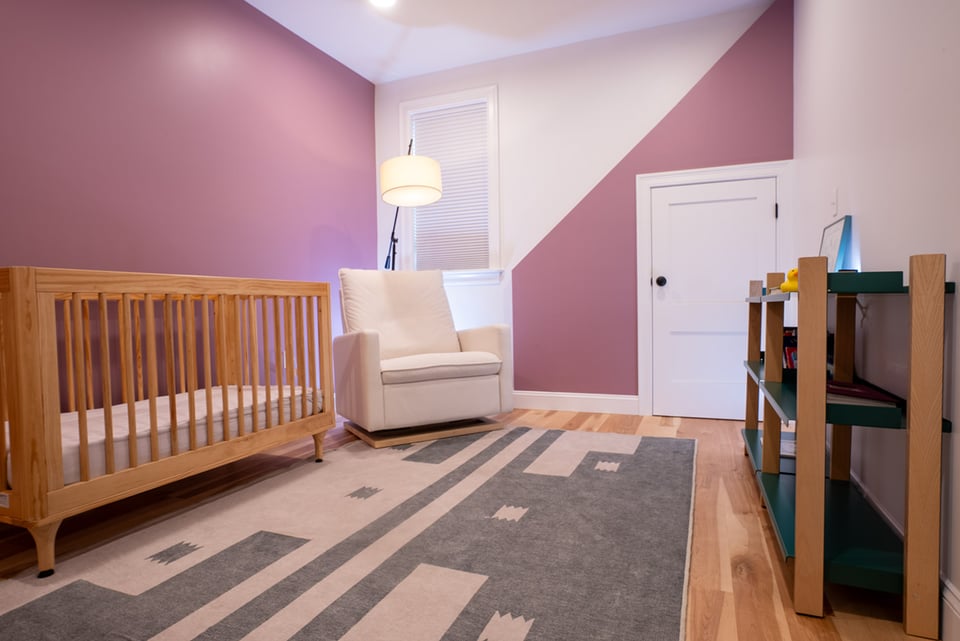 Coastal New Hampshire nursery with a wooden crib, cozy glider chair, and mauve accent wall featuring a geometric paint design