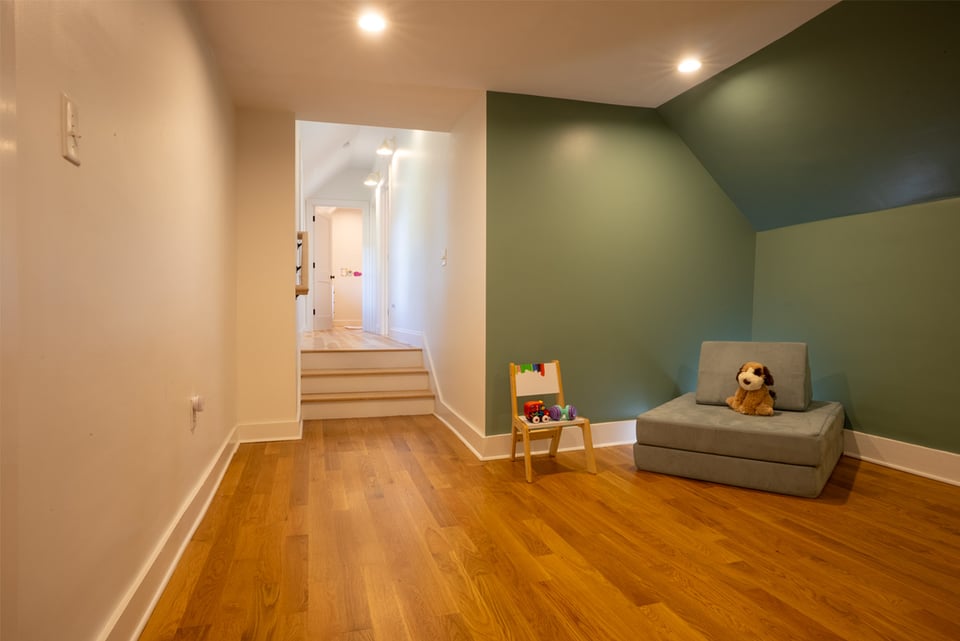 Cozy childrens play nook in New Hampshire with green accent wall, hardwood floors, soft seating, and toys arranged for reading and playtime