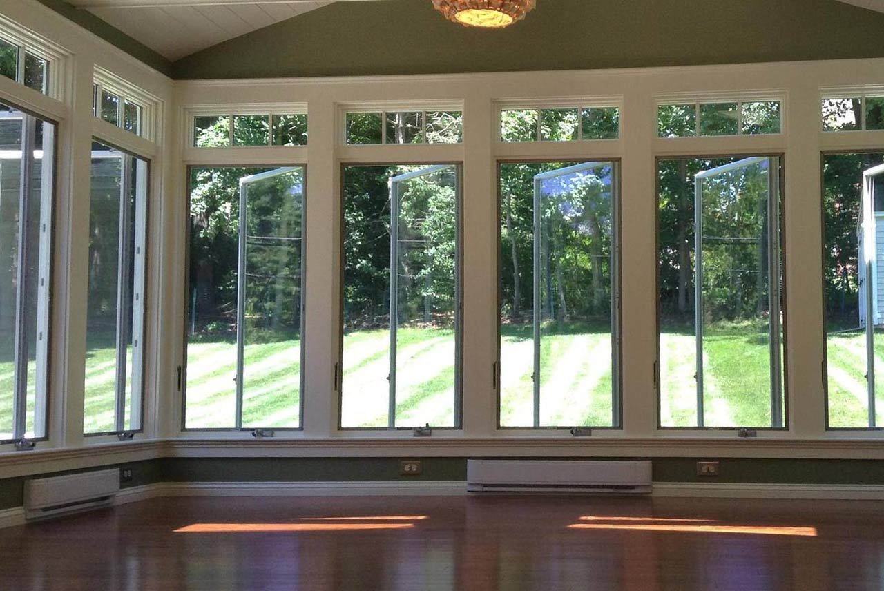Sunroom addition with large windows showcasing a bright backyard, completed-by Oxland Builders in New Hampshire